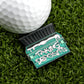 A golf ball sits on green grass next to Logie Joe's Golf’s "Taking Deposits" marker, shaped like a green dumpster with white text and a snow-like line—one of the funniest premium golf accessories around.