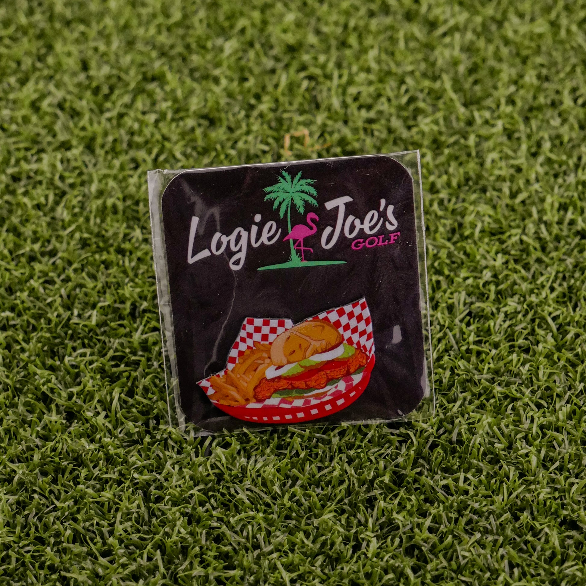 A square sticker featuring Logie Joe's Golf, a palm tree and flamingo logo, and the Breaded Tenderloin Sandwich Basket sits on artificial green grass—perfect for fans of funny golf gear or quirky golf ball markers.