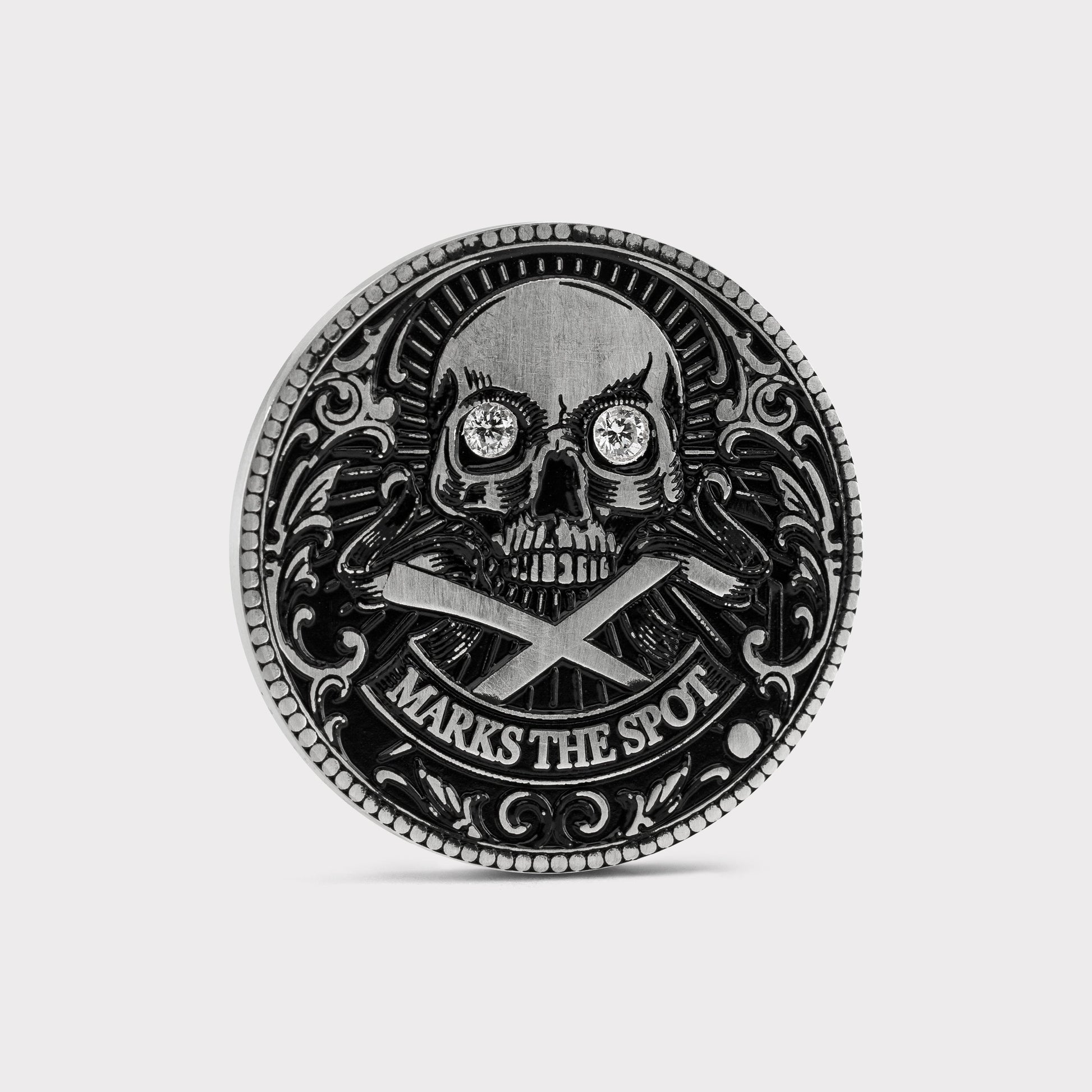 The Omen Classic Antique, Diamond & Silver Edition by Doubloon is a round, metallic golf marker with a lab-grown diamond skull, crossed bones, intricate edge detail, and “MARKS THE SPOT” engraved at the bottom.