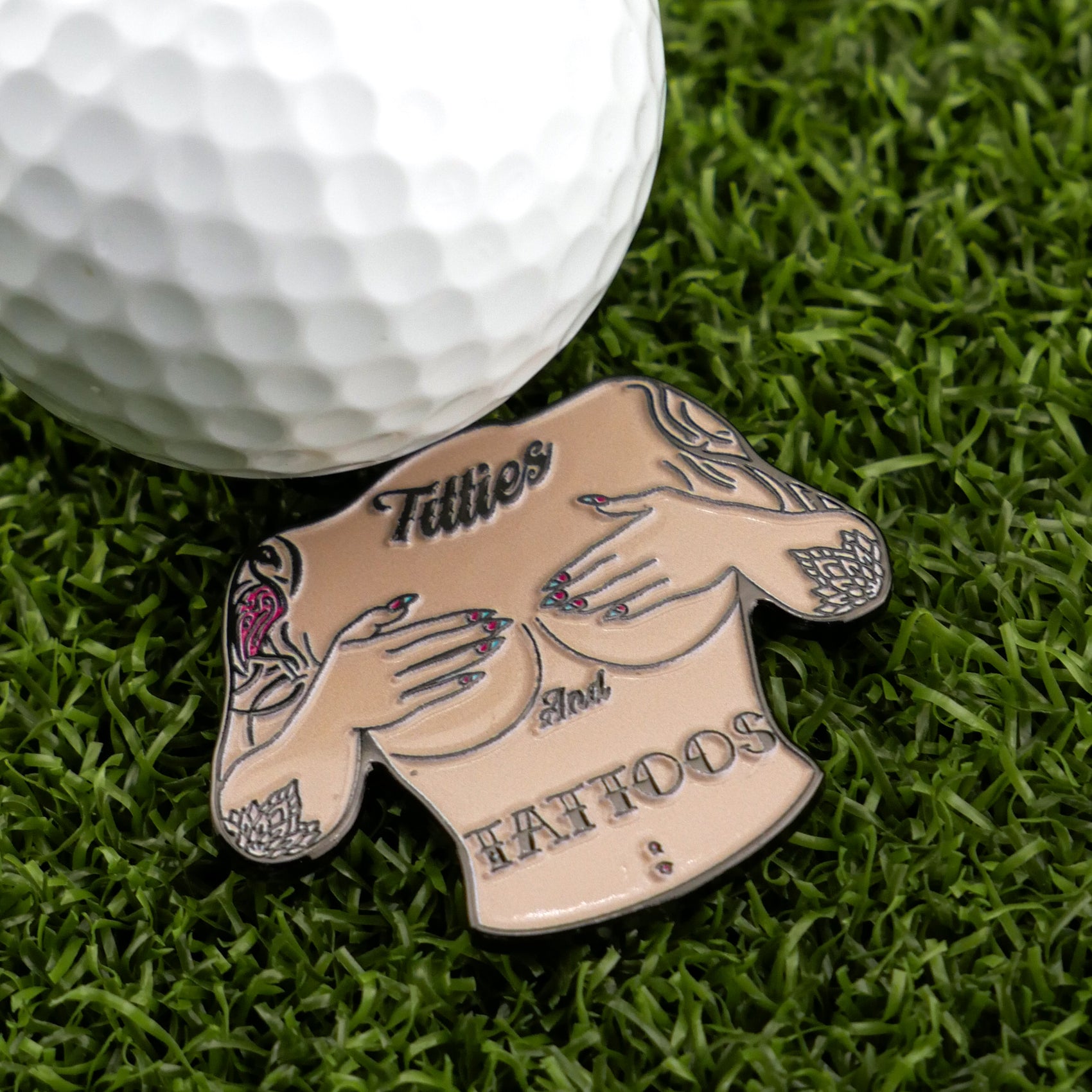 Add fun to your golf game with Logie Joe's Golf Titties & Tattoos ball marker—a premium accessory shaped like a tattooed, topless torso with hands covering the chest and "Titties & Tattoos" lettering.