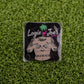 The Titties & Tattoos premium square ball marker by Logie Joe's Golf features a topless tattooed torso, pink flamingo, and palm tree on artificial grass—perfect for those who love funny golf accessories.
