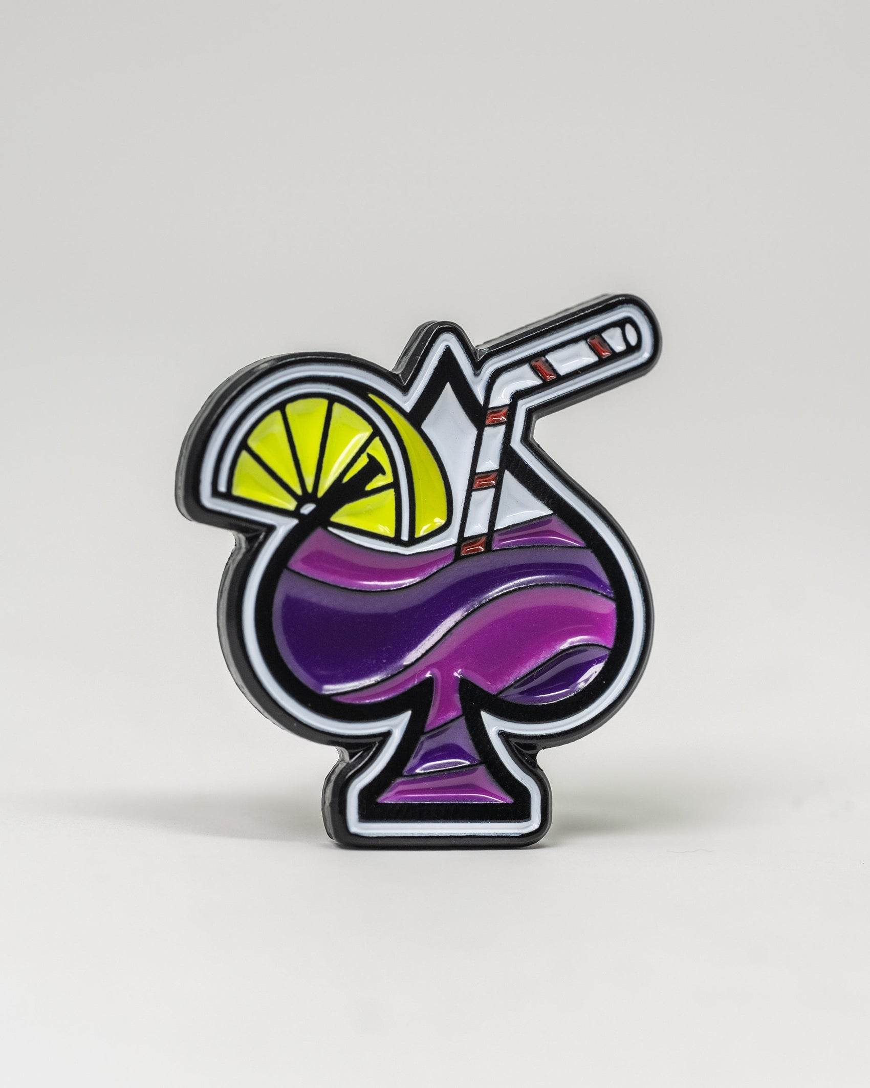 The Transfusion Spade Ball Marker by Pins and Aces is an enamel pin shaped like a spade, featuring a purple drink with a striped straw and lemon slice—ideal for golf fans or unique ball marker collectors.