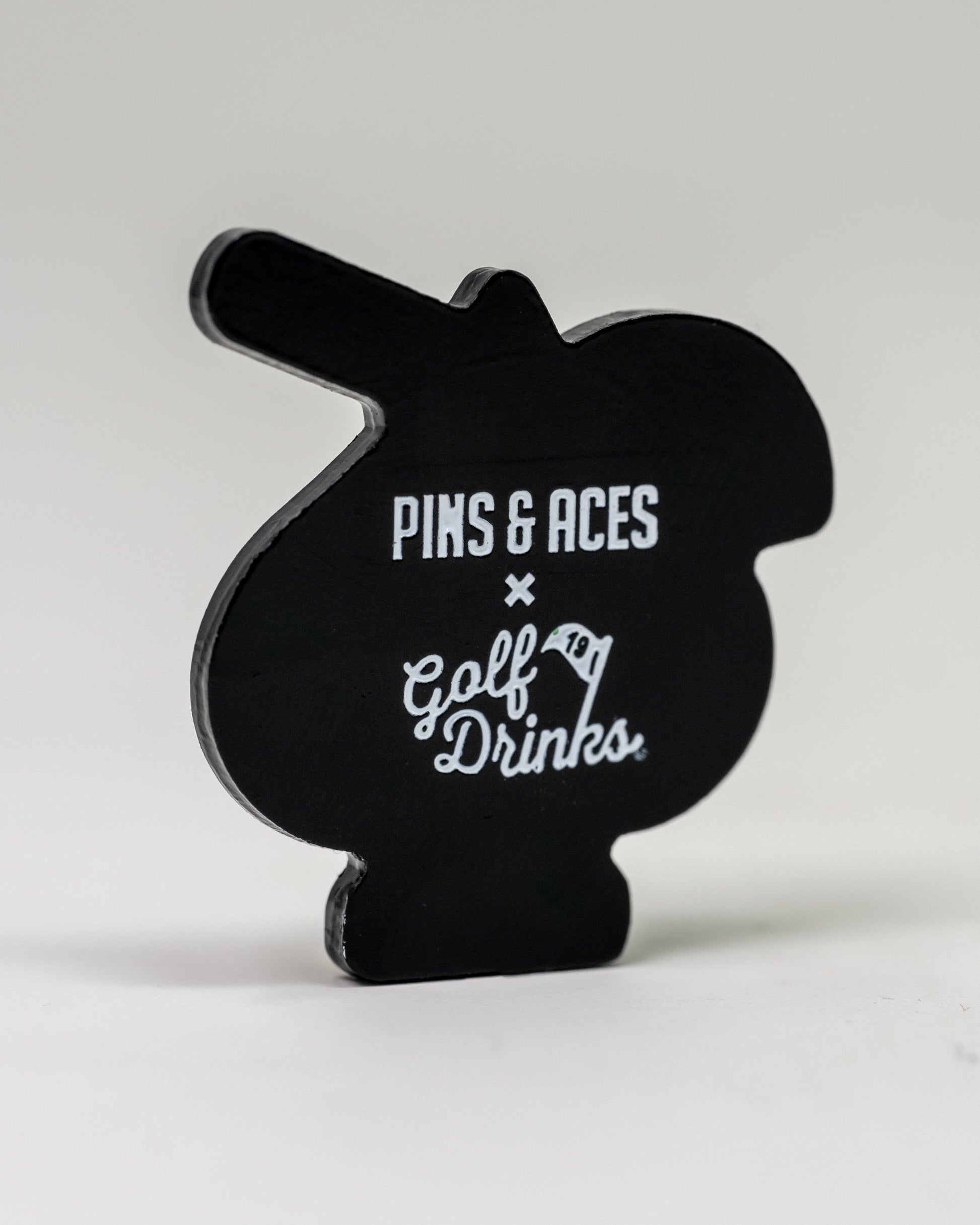 The Pins and Aces Transfusion Spade Ball Marker features a black, cartoon-inspired design with the brand's logo and "Golf Drinks" in white text—an ideal choice for fans seeking a unique golf ball marker.