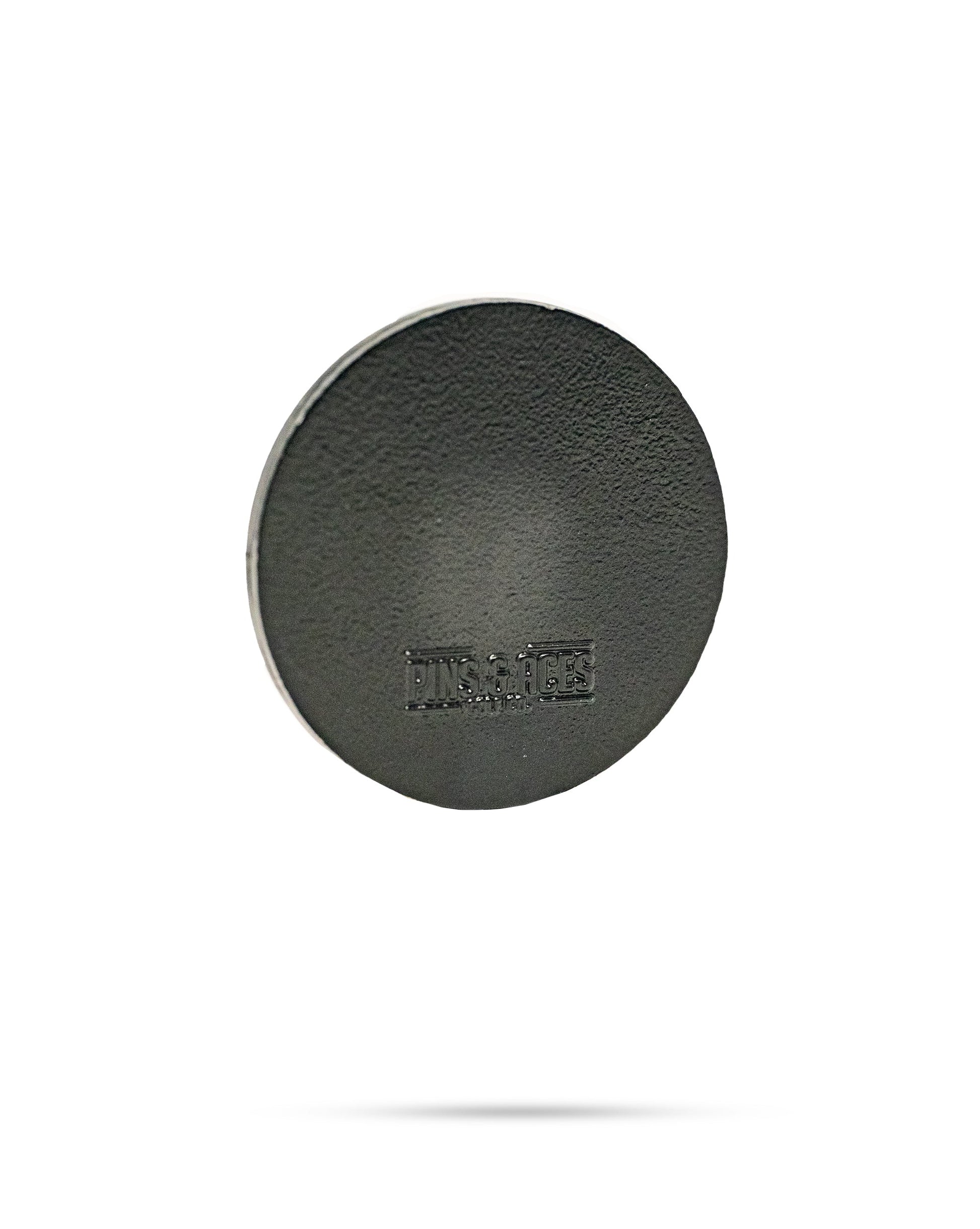 A round, flat, black textured metal 47 Ball Marker by Pins and Aces, featuring DINSAUCE imprinted on its surface, floats against a white background with a faint shadow. This limited edition item is ideal for collectors and enthusiasts.
