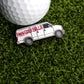 A golf ball sits on green grass next to the Logie Joe's Golf Free Golf Ball Van Ball Marker, shaped like a white van with "FREE GOLF BALLS" in red—a playful addition to your golf gear.