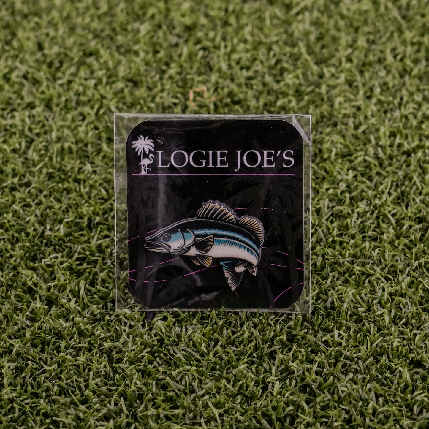 A square sticker featuring a walleye fish illustration and Logie Joe's Golf text on a dark background, set on green turf—ideal for golf enthusiasts seeking fun accessories or premium ball marker inspiration.