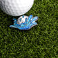 A close-up of a golf ball on artificial grass alongside the Ballmarkers.com Water Ball Ball Marker, a playful accessory shaped like a splash—perfect for golfers with a sense of humor about water hazards.
