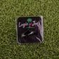 A black square pin from Logie Joe's Golf, named Killer Whale, features playful animal designs and is a humorous golf accessory—ideal as a ball marker—shown on green artificial grass.