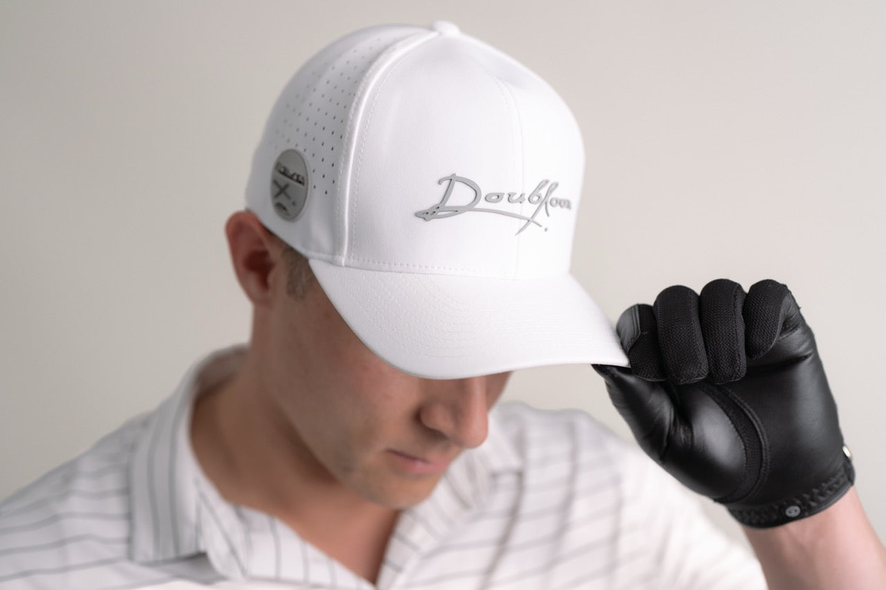A person in a white "Darkfour" cap, black golf glove, and white collared shirt tilts their cap down, partially hiding their face, while holding Doubloon’s The Omen Classic Antique, Diamond & Silver Edition sterling silver golf ball marker.