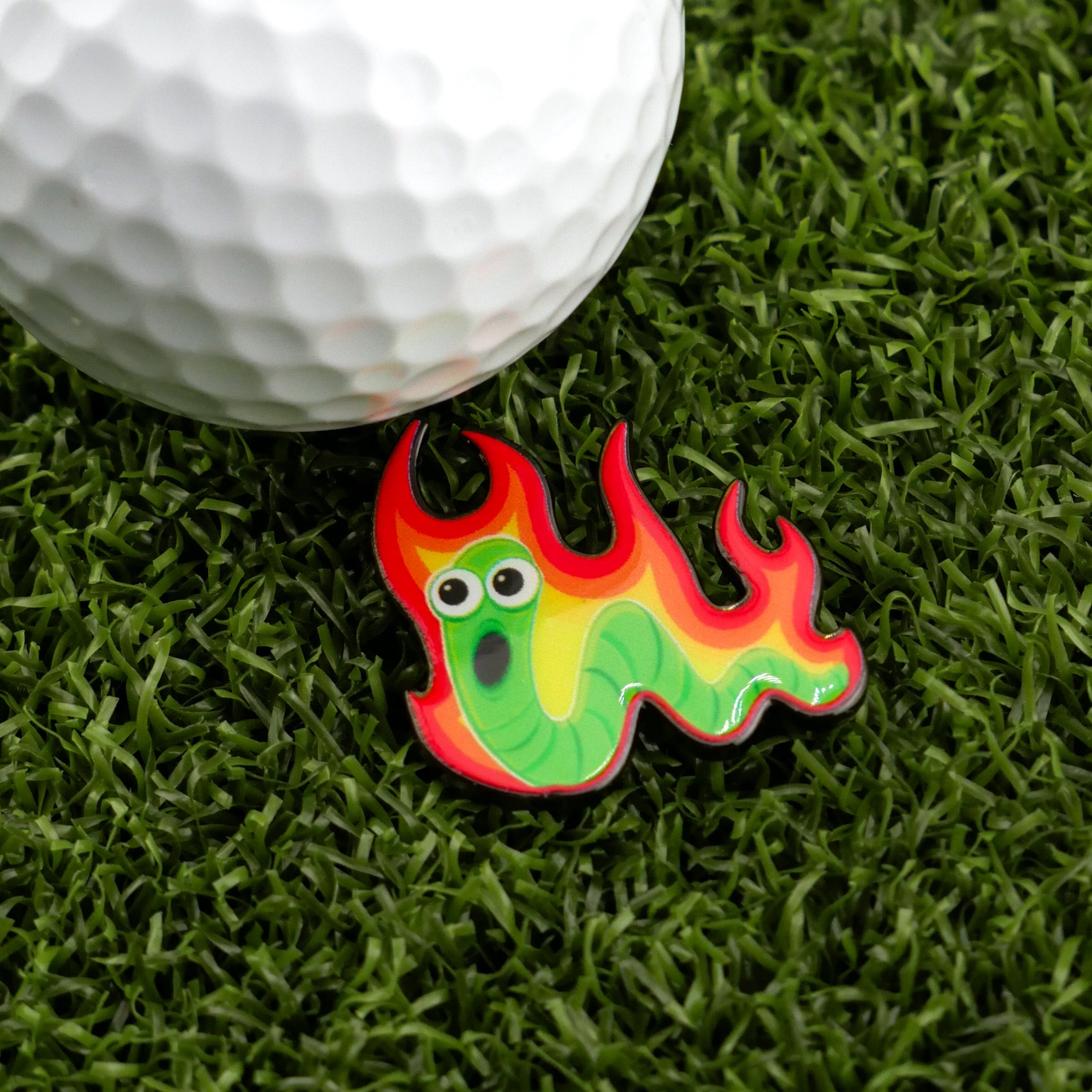 The Worm Burner by Logie Joe's Golf is a vibrant golf ball marker shaped like a green worm with big eyes and fiery red-yellow flames—an ideal pick for anyone who loves unique golf accessories.