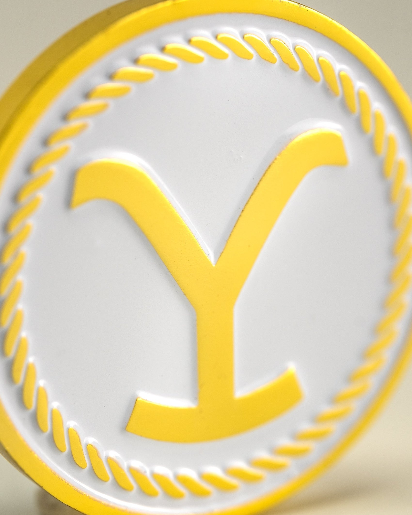 The Pins and Aces Yellowstone Ball Marker features a round, white and yellow design with a raised yellow Y and rope-like border—a must-have golf accessory for any player.