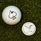 A golf ball with a black spade sits next to the Yellowstone Ball Marker—with its Y-shaped design—by Pins and Aces, both on green turf. This unique golf accessory set is a highlight of the collection.