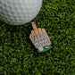 A golf ball sits on green grass beside the Logie Joe's Golf Zero Putts Given Ball Marker, shaped like a hand making a rude gesture—a hilarious, unique accessory and fun golf ball marker for your next round.