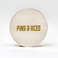 A round, metallic 6 Milly - Cinnamon Ball Marker by Pins and Aces features gold engraved branding and a smooth enamel finish, shown against a plain white background.