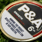 A close-up of the Pins and Aces 6 Milly - Smooth Ball Marker on green grass, built for magnetic surfaces, and featuring a warning: This product results in birdies. Birdies can be very addictive.