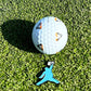 A ChunkMan Ball Marker by Grunk Dolfer rests on green grass, featuring black and orange details. Below is a blue silhouette keychain mid-jump with a golf ball—an eye-catching accessory and unique golf gift.