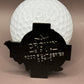 A white golf ball is partially covered by a black Donut A Hole Ball Marker from Crown Golf Designs, engraved with CROWN ROYAL FOOD TOUR SERIES 2014 and a crown logo.