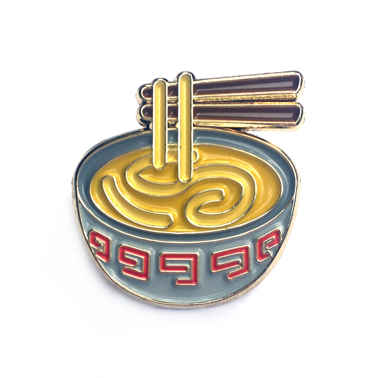 The Kolorspun Ramen Noodles Golf Ball Marker is a decorative enamel pin featuring yellow noodles, chopsticks, and a red geometric pattern on a blue bowl—making it the perfect unique golf gift.