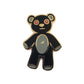 The Kolorspun Teddy Bear Golf Ball Marker features a black bear with red X eyes, a light gray belly, and gold outlines on white. Its magnetic back and unique stitched look make it a cute, quirky golf gift.