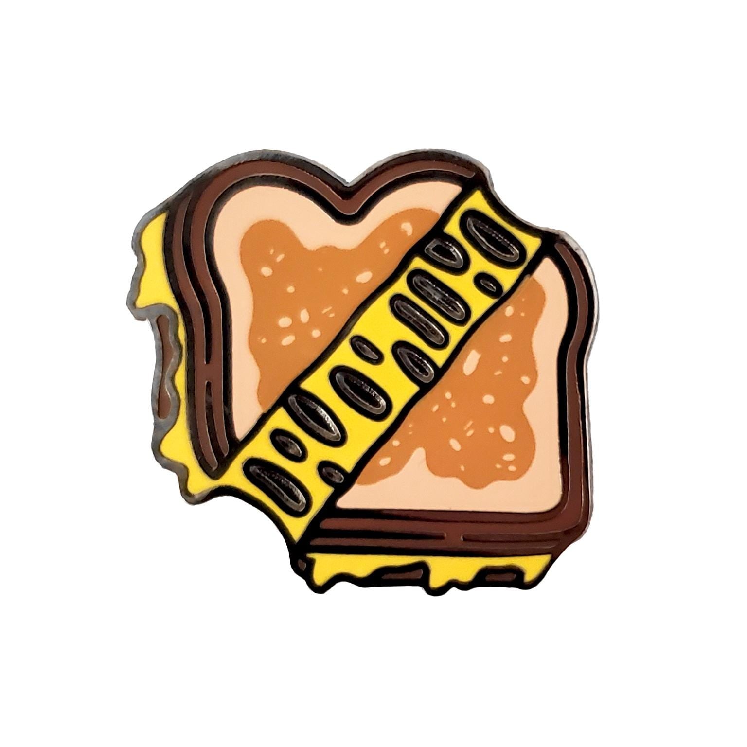 The Kolorspun Grilled Cheese Sandwich Golf Ball Marker is a cartoon-style enamel pin—perfect as a quirky custom marker or unique golf gift for fun-loving players.