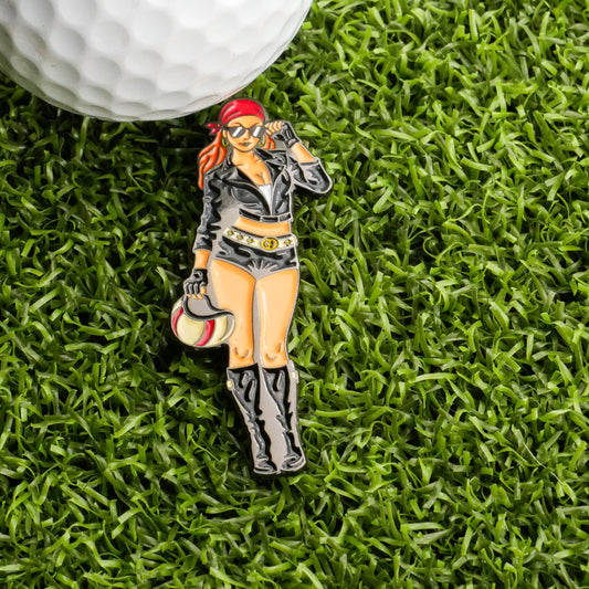 A golf ball and the Biker Girl Ball Marker by Ballmarkers.com, featuring a woman in black with sunglasses and helmet, displayed on green artificial grass.
