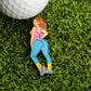 The Aerobic Workout Girl Ball Marker from Ballmarkers.com features a cartoon woman in vibrant fitness wear, posing on green turf near a white golf ball—perfect for adding retro gym vibes to your golf accessories.