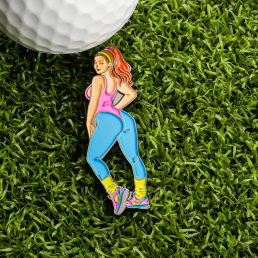 The Aerobic Workout Girl Ball Marker from Ballmarkers.com features a cartoon woman in vibrant fitness wear, posing on green turf near a white golf ball—perfect for adding retro gym vibes to your golf accessories.