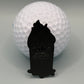 A UPS Dumpster Fire golf ball from Crown Golf Designs sits on a gray surface with a small, magnetic, crown-shaped marker featuring a raised crown design placed in front of it.