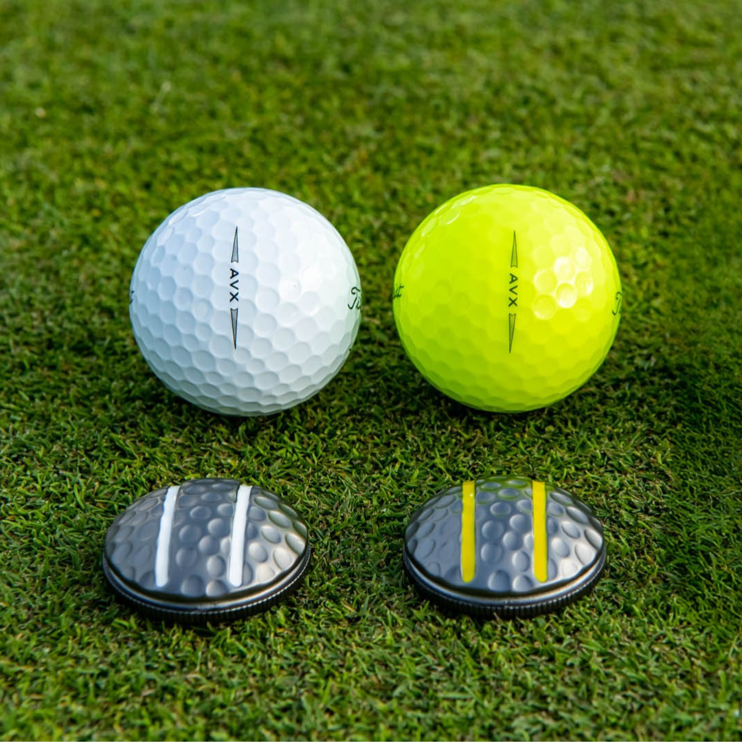 Two OnPointGolf.us Two Rail Ball Markers, one for a white ball and one for a yellow ball, sit on grass, each matching the alignment lines of its golf ball—creating a practical alignment tool and putting aid.