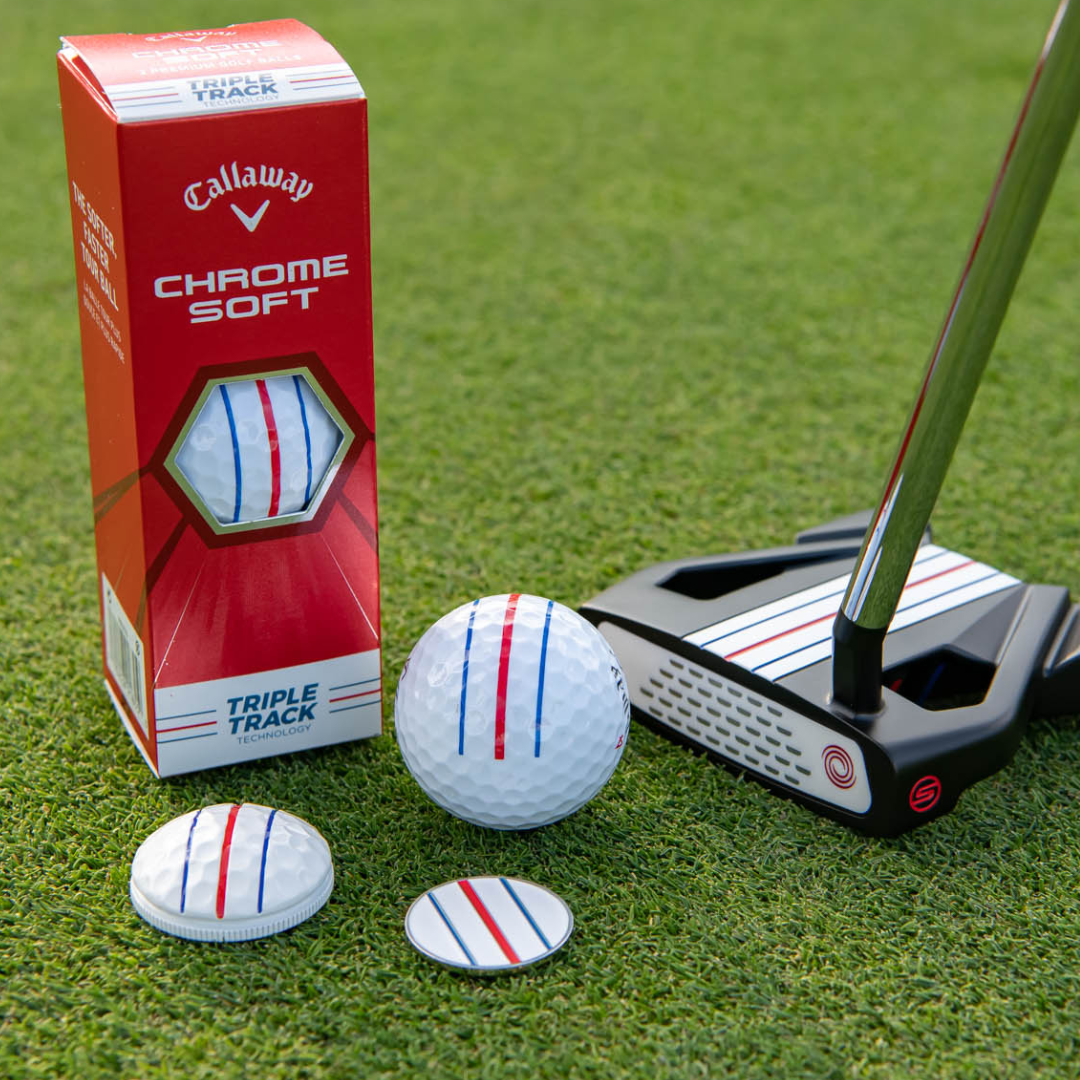 An OnPointGolf.us Three Rail Ball Marker sits on grass next to a putter and golf ball, all featuring red and blue alignment lines—ideal putting aids for perfect alignment.