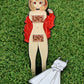The Japanese Anime golf ball marker from Ballmarkers.com features a girl with bear-ear buns, red jacket, and pixelated bars on grass. A separate white dress pin lies beside her, resembling a divot tool.