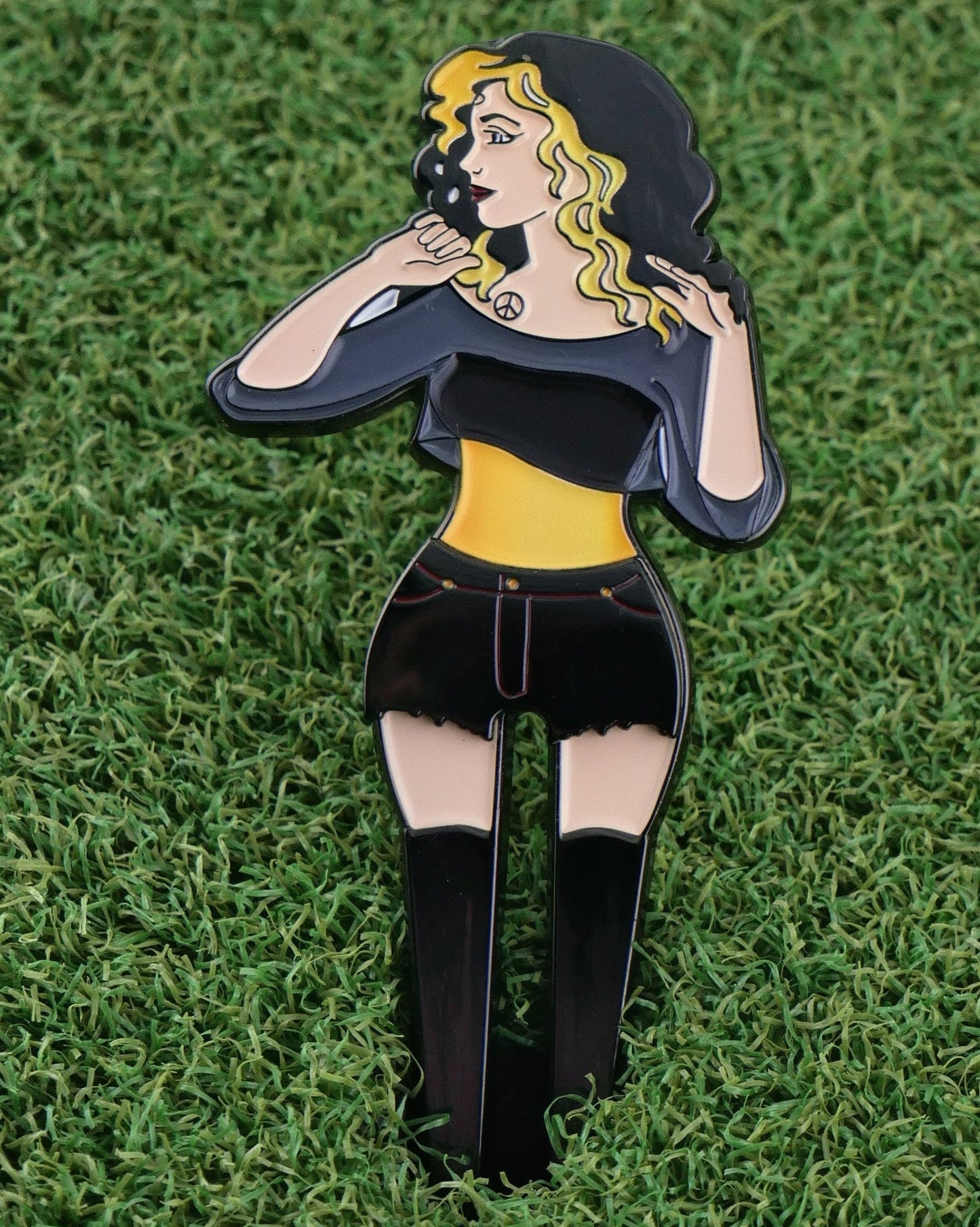 Lady Boy 2.0 by Ballmarkers.com is a cartoon-style enamel pin featuring a woman with black and yellow hair, chic outfit, and boots—displayed on green turf, it's the perfect golf accessory for stylish fans.