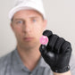 A person in a white cap and gray shirt, wearing a black glove, holds up Doubloon's The Silver Omen Antique, Color Edition golf ball marker—a pink coin with graphic design—while their face is out of focus in the background.